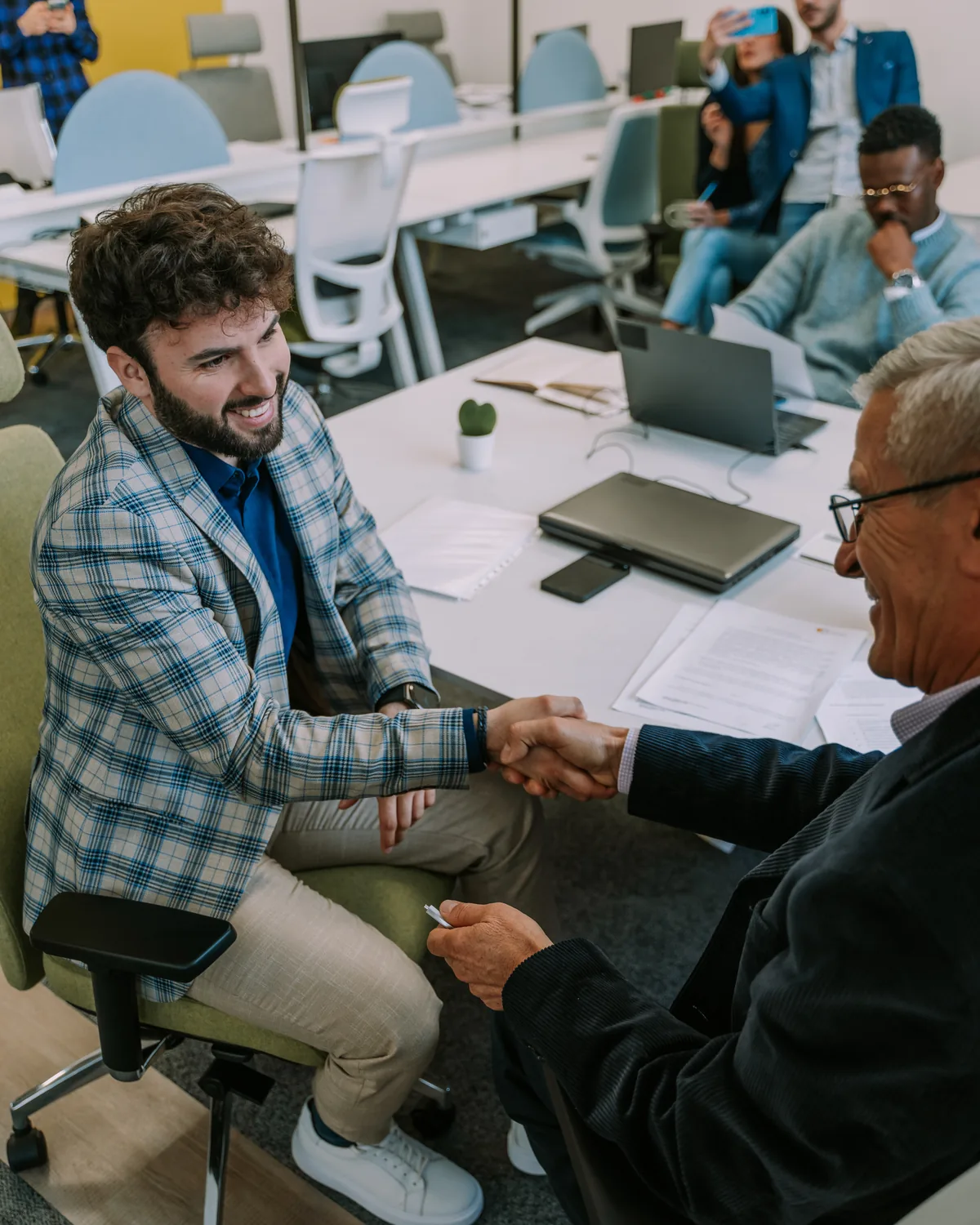 Two business partners shaking hands across a meeting table.
