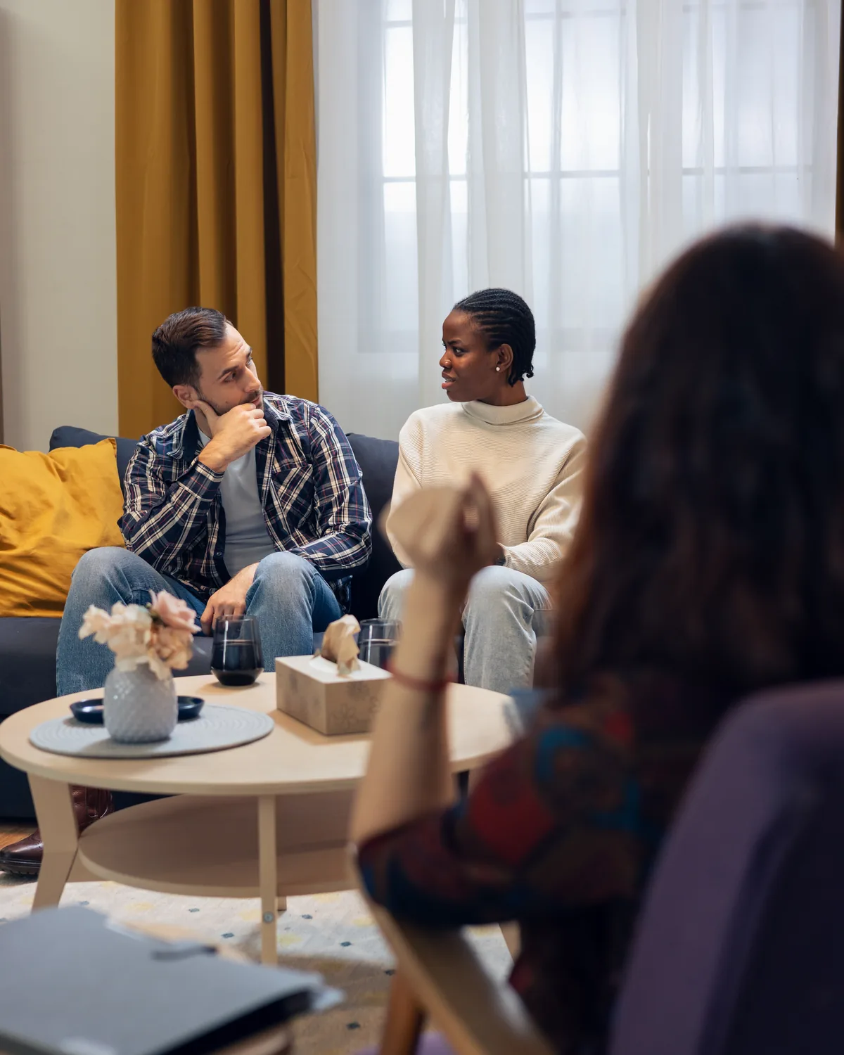 A couple talking with a mediator across a coffee table in a bright room.